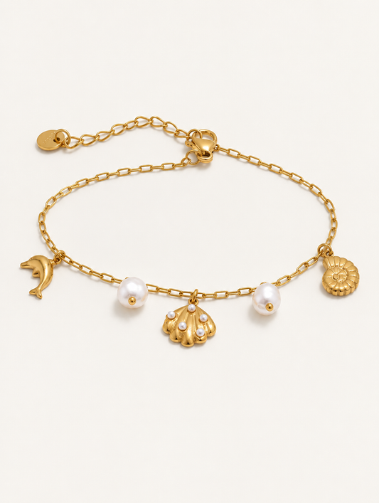 Gold-tone ocean charm bracelet with dolphin, shells and pearls on a neutral background