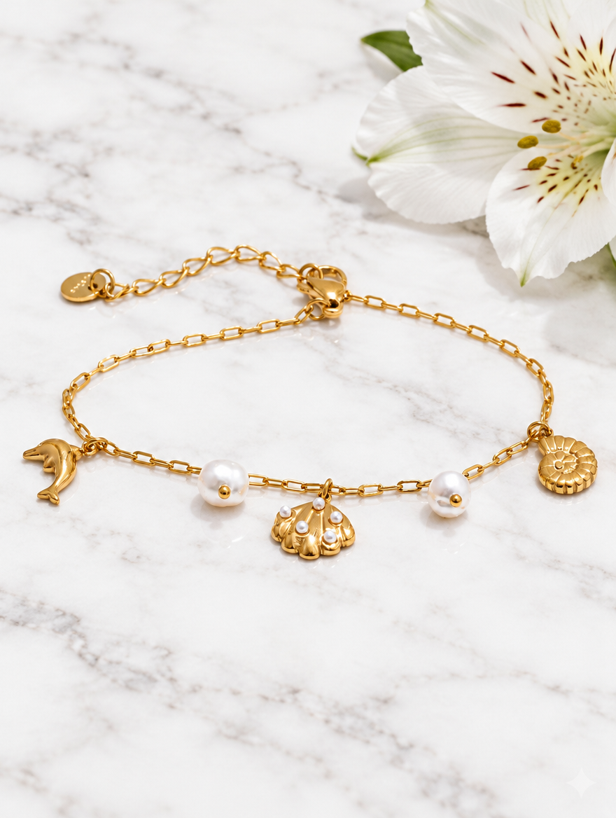 Gold-tone ocean charm bracelet beside a white flower on marble