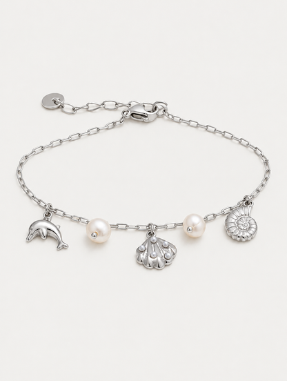 Silver-tone ocean charm bracelet with dolphin, shells and pearls on a neutral background