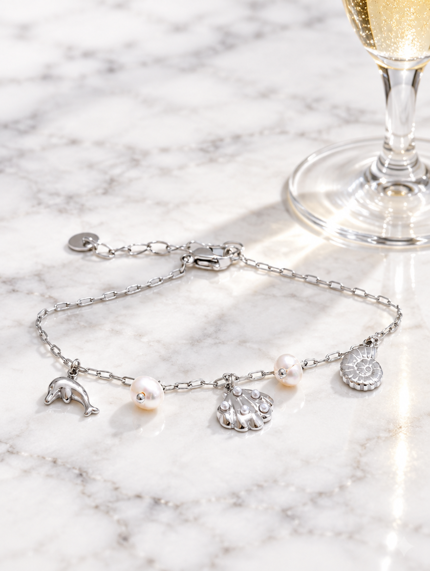 Silver-tone ocean charm bracelet beside a champagne flute on marble
