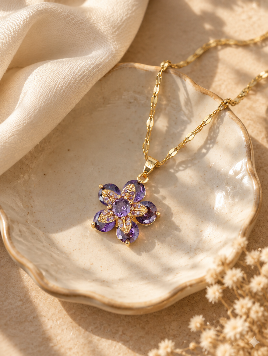 Gold purple flower pendant necklace on a ceramic dish beside a folded cream scarf