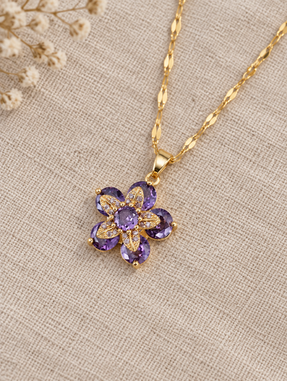 Gold purple flower pendant necklace lying flat on linen