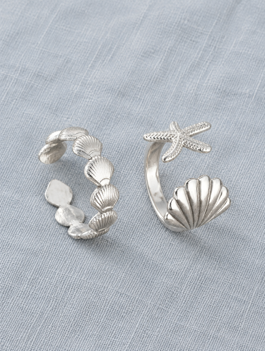 Set of two silver shell and starfish rings resting on a soft textured surface