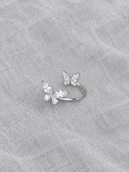 Silver twin butterfly sparkling open ring resting on a soft textured surface