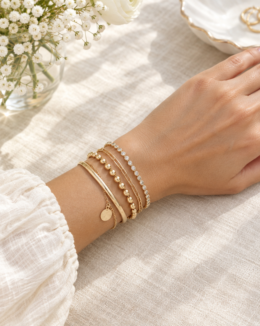 Wrist wearing stacked gold-tone bracelets on linen
